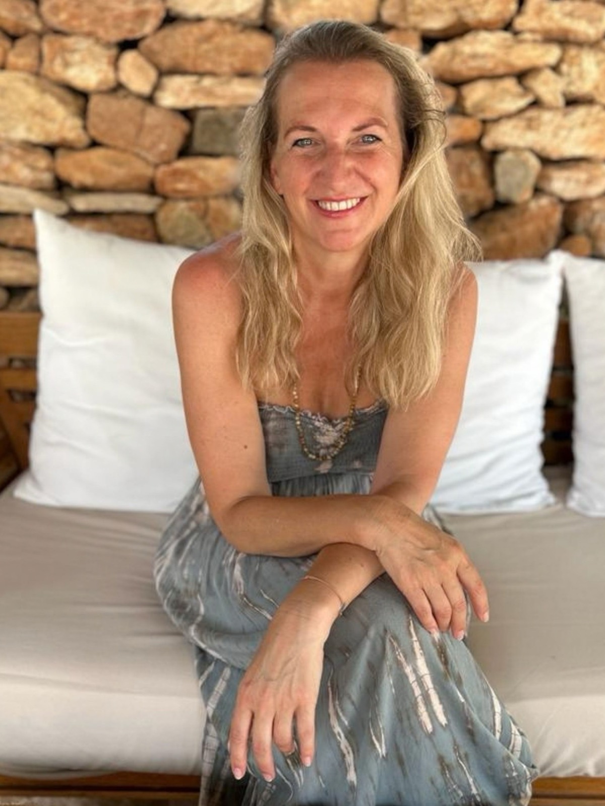 Maria Peischl lachend vor einer sonnigen Natursteinmauer